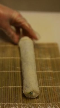 Eller suşiyi bambu hasırında pirinç ve sebze kullanarak sarıyor. Mutfakta basit aletler ve malzemeler var. Bu Paskalya tatili sırasında gerçekleşir..