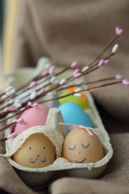 Paskalya yumurtaları yüzlerle süslenmiş birkaç yumurtanın içinde düzenlenir. Bahar çiçekleri yakınlarda. Bu dekor mevsimin neşesini yakalar..