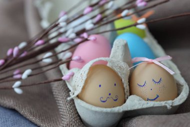 Bir karton süslenmiş Paskalya yumurtalarını açık renklerle saklar ve içinde basit yüzler bulunur. Yakınlarda, küçük tomurcuklu ince dallar Paskalya bayramını daha da güzelleştiriyor..