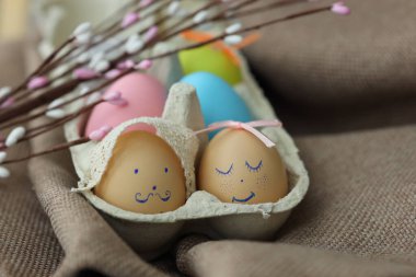 Renkli Paskalya yumurtaları kahverengi bir bezin üzerindeki yumurta kutusuna yerleştirilir. Bazı yumurtaların yüzleri ve kurdeleleri vardır. Dekoratif çiçekler sahneye cazibe katar..