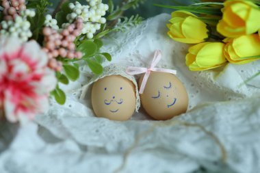 Madalyalı iki Paskalya yumurtası bir örtü ve çiçeklerle birlikte yerleştirilir. Bir yumurtanın gülen bir yüzü var ve diğeri uyuyor gibi görünüyor. Bu sahne Paskalya için neşeli bir an..