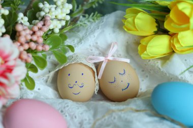 Renkli çiçekler ve ek yumurtalar arasında beyaz bir bez üzerinde duran iki süslü yumurta. Bu sahne baharda Paskalya kutlamalarının neşesini yakalar..