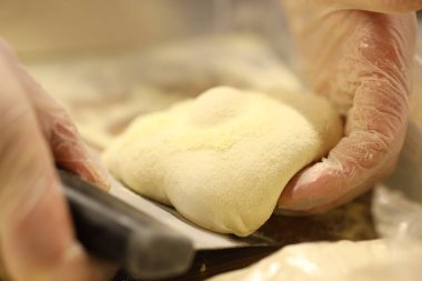 Bir fırıncı eldiven giyerken hamuru kazıyıcı ile şekillendiriyor. Dekor bir mutfak ve etkinlik de sabahın erken saatlerinde pişirme sürecinin bir parçası..