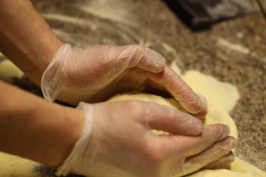 Eldiven giyen eller mutfaktaki un tozlu tezgahta hamur işi yapar. Bu süreç ekmek ya da makarna yapma becerisini ve çabasını gösteriyor..