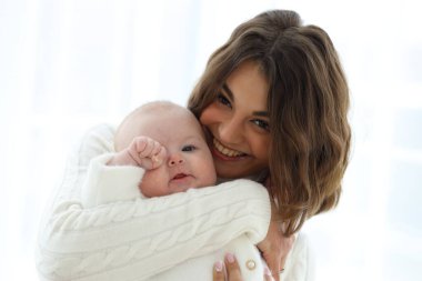 Genç bir anne bebeğini kollarına alır, hem gülümser, hem de sıcak bir bağı paylaşır. Dekor basit ve parlak. İçerde rahat bir atmosfer var..