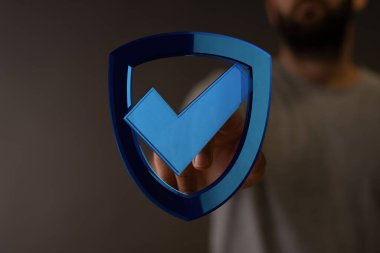 Güvenlik onayı için mavi işaretli kalkan sembolü tutan adam.