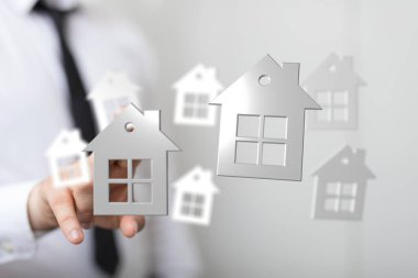 Yüzen ev simgelerini tutan, ev sahipliğini ve hayalleri temsil eden bir adam.