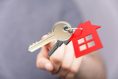Gri arka planda kırmızı ev şekilli anahtarlığı olan ev anahtarı.