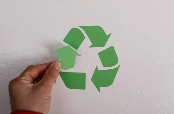 Hand Placing Recycling Symbol Against a Textured White Wall