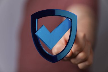 Güvenlik ve onay işaretli mavi bir kalkanı işaret eden kişi..