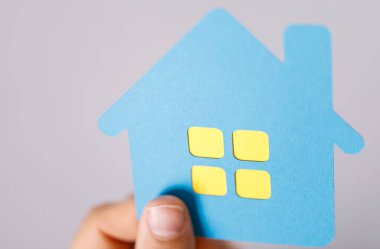 Sarı pencereli mavi bir kağıt evi el ele tutuşmak: emlak kavramı.