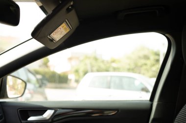 Bir arabanın güneşliği açık. Otoparkın bulanık bir görüntüsü var.