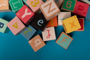 Mavi bir yüzeye dağılmış renkli alfabe blokları.