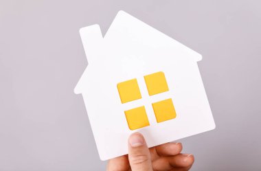 Evi ve aileyi sembolize eden bir kağıt evi tutan.