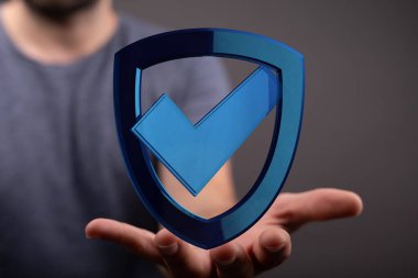 Üzerinde kontrol işareti olan mavi bir kalkan tutan bir adam.