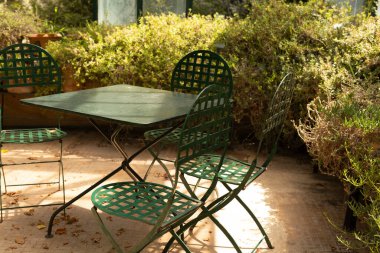 Boş yeşil bir masa ve dışarıda yeşil sandalyeler oturuyor.
