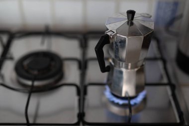 Gümüş bir kahve demliği, ocağın üzerinde mavi bir alev ile duruyor. 