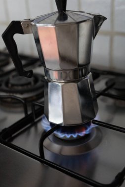 Gümüş bir kahve demliği, ocağın üzerinde mavi bir alev ile duruyor. 