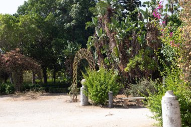 Tahta kemerli bir kemer, taştan bir bankla yemyeşil bir bahçede duruyor. 