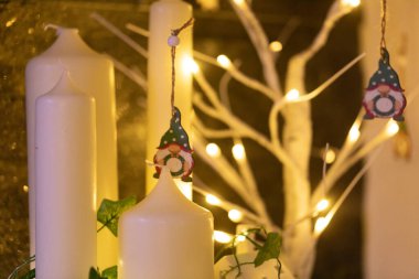 Cüce süslemeli beyaz mumlar, sıcak ışıklar ve yeşillik. Şenlikli kış sezonu dekorasyonu.