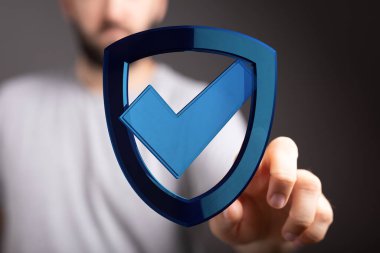 Güvenlik ve veri koruması için kontrol işaretli mavi kalkan sembolü tutan adam.