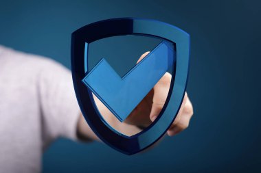 İşaretli bir kalkan simgesini tutan el, başarı ve güvenliği temsil ediyor.