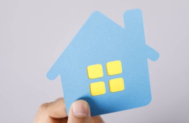 Elinde sarı pencereli mavi bir kağıt ev var.