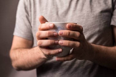 Elinde bir fincan kahve tutan, elinde sıcak içkinin tadını çıkaran bir adam.