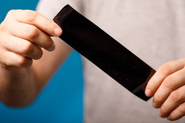 Elleri mavi arkaplanda siyah bir bant tutuyor.