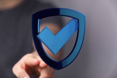 Üzerinde işaret işareti olan mavi bir kalkanı işaret eden kişi..