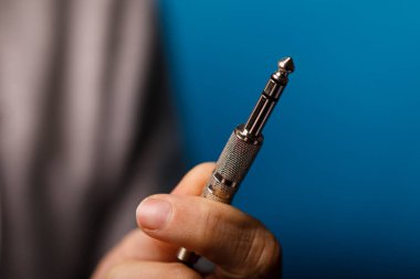 Mavi arka planı olan metal bir ses krikosunu tutan bir elin yakın çekimi