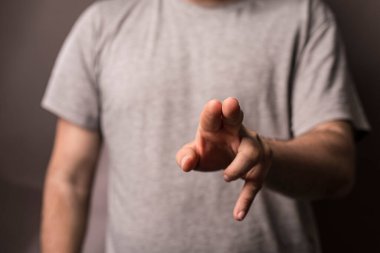 Human hand pointing towards viewer with grey shirt background