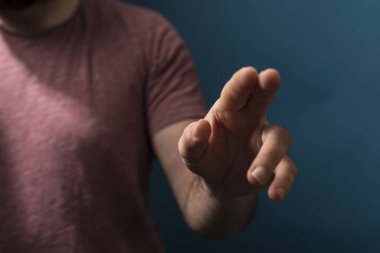 Man's hand pointing at the viewer with a blue background, close up