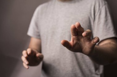 Elle hareket eden bir adam, bir şeyi kavramak için uzanıyor, kapalı bir yerde, gri gömlekli..