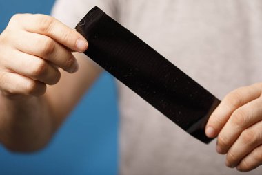 Elleri mavi arkaplanda siyah bir bant tutuyor.