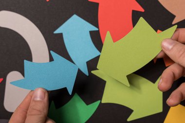 Koyu bir arkaplan üzerinde insan eliyle tutulan renkli kağıt oklar.