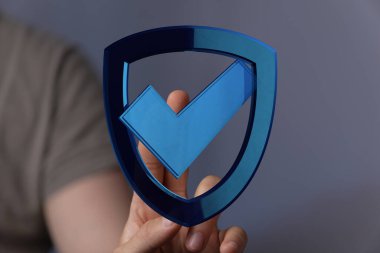 Gri bir arkaplan üzerinde işaret sembolü olan bir kalkan simgesini tutan