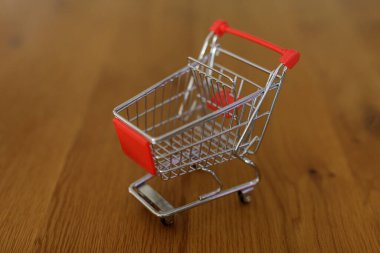 Ahşap yüzeyinde kırmızı saplı küçük alışveriş arabası.