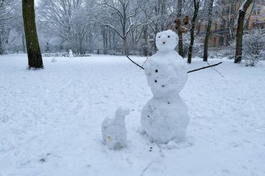 Grimmstrasse parkında kar fırtınalı bir kış gününde Berlin Kreuzberg 'de kardan adam ve kar köpeği. Kolları dal, burnu havuç gibi..