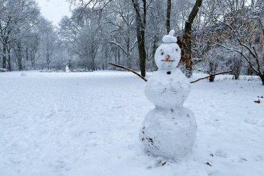 Grimmstrasse parkında kar yağışlı bir kış gününde Berlin Kreuzberg 'de kardan adam. Kolları dal, burnu havuç gibi..