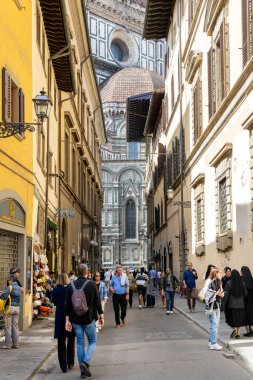 Florence, Italy - May 11th, 2025: Tourists walk along a narrow street in the historic center, with a stunning rear view of the Cathedral