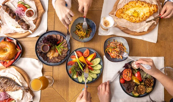 Dining table with various dishes top view, group of people dining together. People use cutlery.