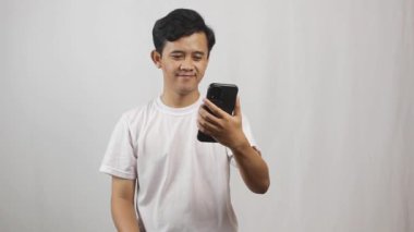 Asyalı adam beyaz tişört giyip yakın arkadaşıyla video görüşmesi yapıyor.
