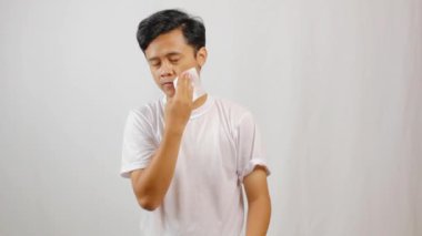 Yorgun Asyalı adam beyaz arka planda izole edilmiş dokularla yağlı yüzünü siliyor.