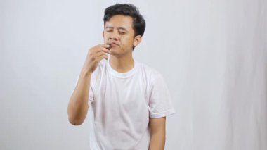 Asyalı adam beyaz arka planda küçük çikolatalı pasta yemekten hoşlanıyor.