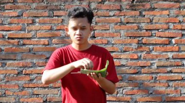 Fıstık sosuna bulanmış, muz yaprağı kabına sarılmış, eski tuğla duvar arkasına izole edilmiş, Lontong ve tavuk yiyen Asyalı bir adam.