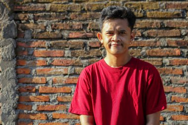 Asyalı bir adam gülen yüzünü sabah güneşine maruz bırakmış tuğla duvarlı arka plan.