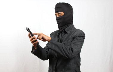 Kar maskesi takan ve siyah takım giyen bir bilgisayar korsanı, kurbanın verilerini akıllı telefonla hackliyor.