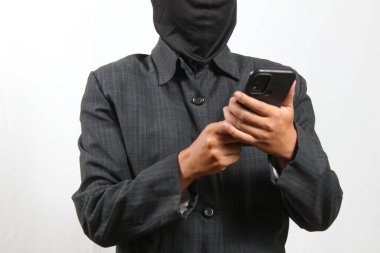 Kar maskesi takan ve siyah takım giyen bir bilgisayar korsanı, kurbanın verilerini akıllı telefonla hackliyor.