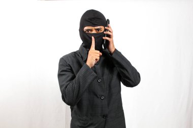 Siyah takım elbiseli ve maskeli hacker sessiz işareti yaparken kurnaz tehditler savuruyor.